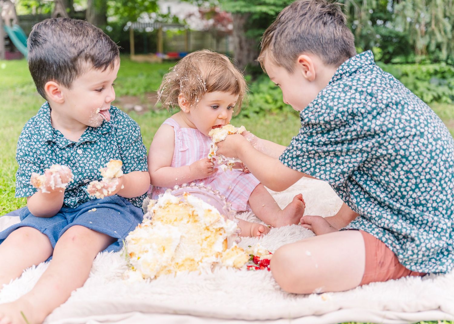 Children playing with cake during outdoor celebration on white blanket.