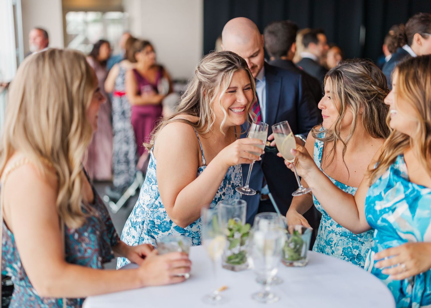 Friends in coordinating blue floral dresses toast with wine glasses at an elegant party gathering.