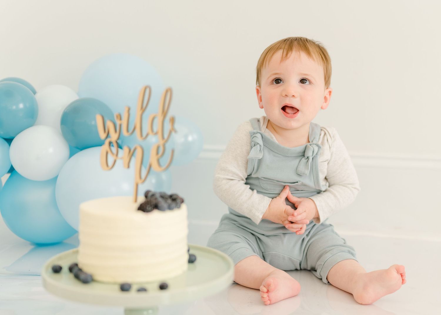 First birthday celebration setup with blue and white balloons, white cake, and 'wild one' gold topper decoration.