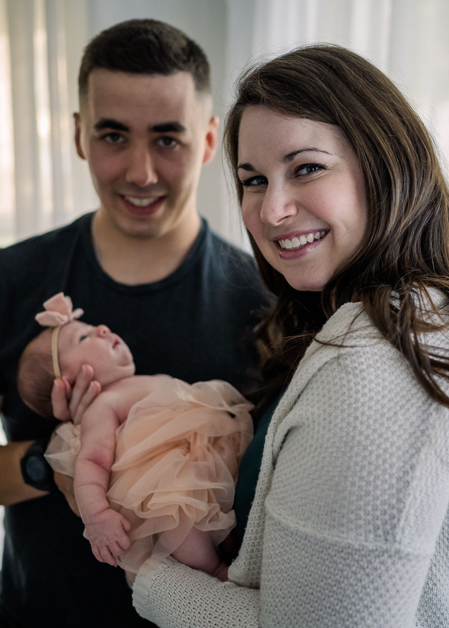 Joyful indoor family portrait with newborn in pink outfit.