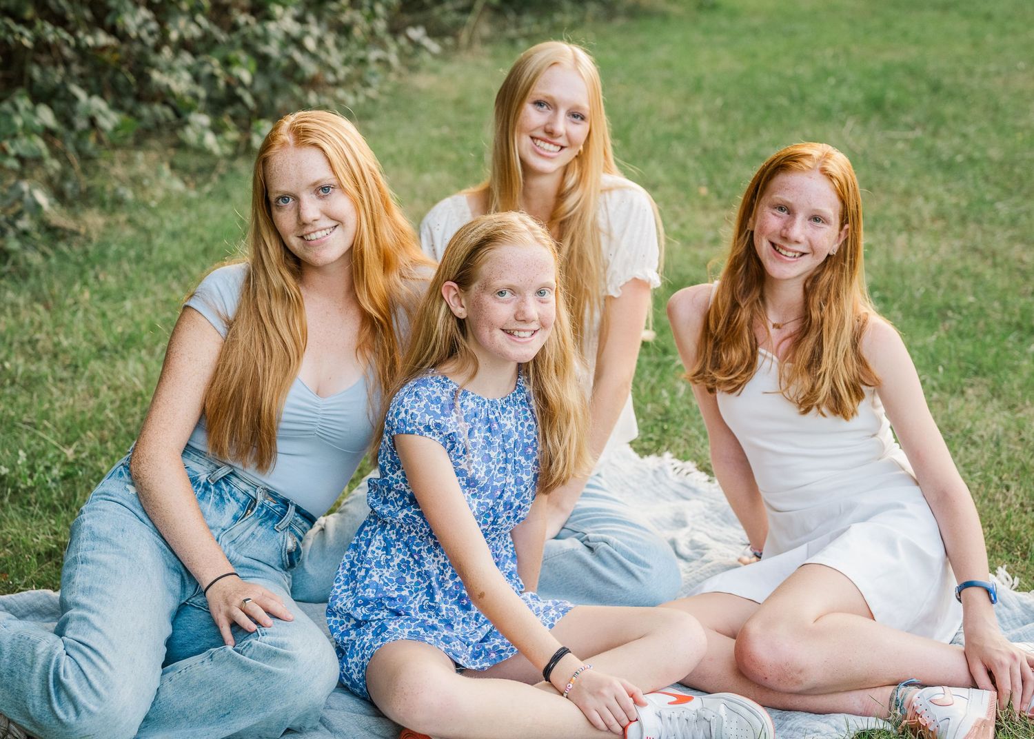 Group portrait of four redheaded siblings sitting together on grass during golden hour.