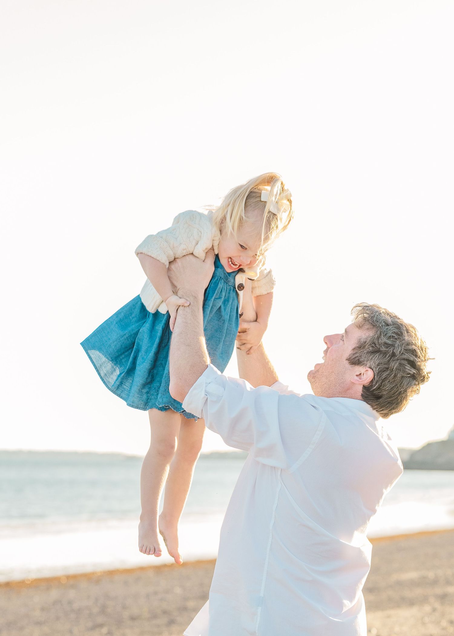 Playful moment on the beach as a child is lifted into the air at sunset.