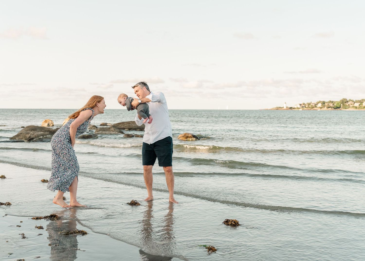 Two people in casual attire dance playfully together on a rocky beach at sunset with ocean waves in the background.