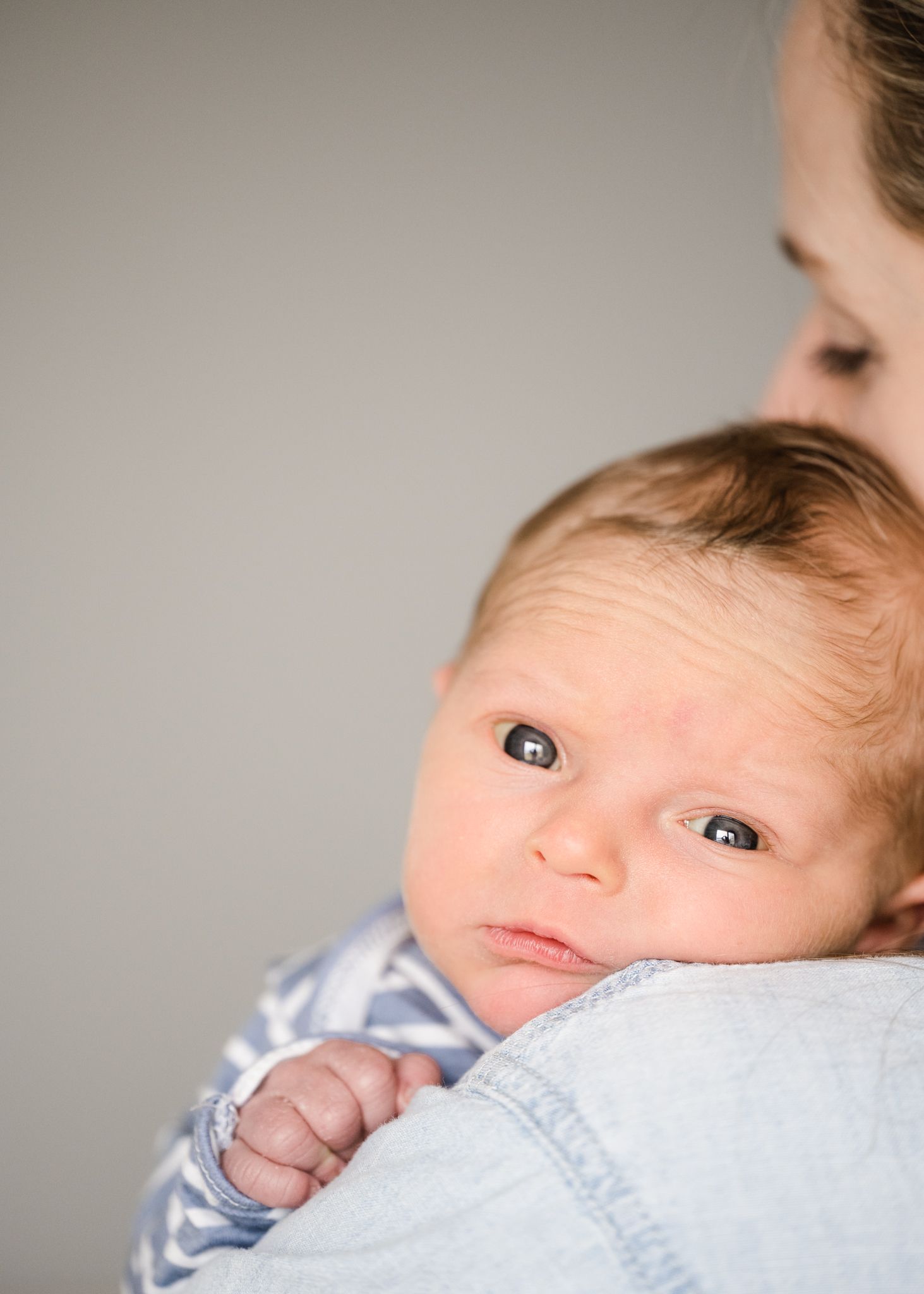Close up of baby resting on parent's shoulder in soft lighting.
