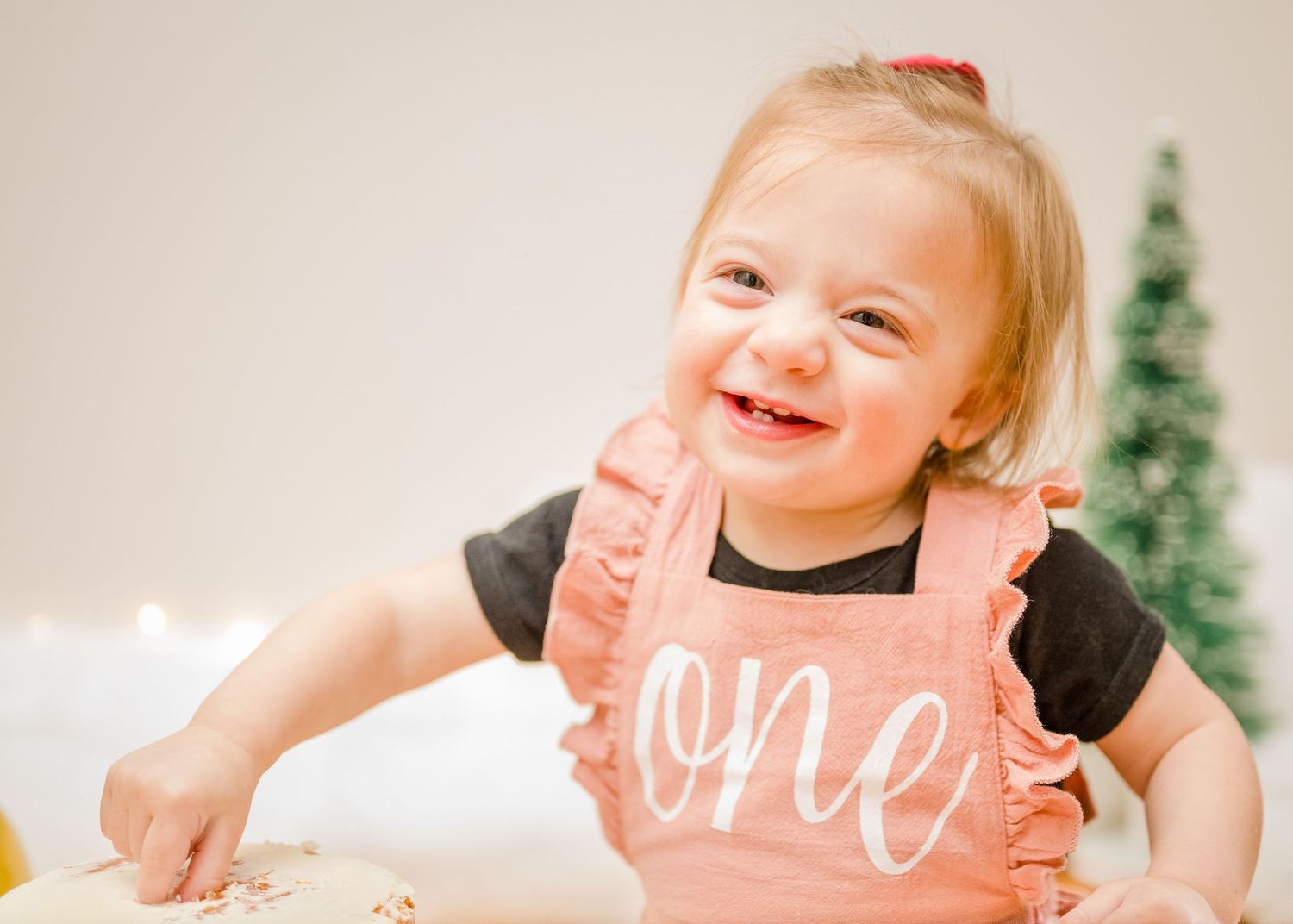 Toddler in pink overalls giggles while sitting at a decorated holiday table.