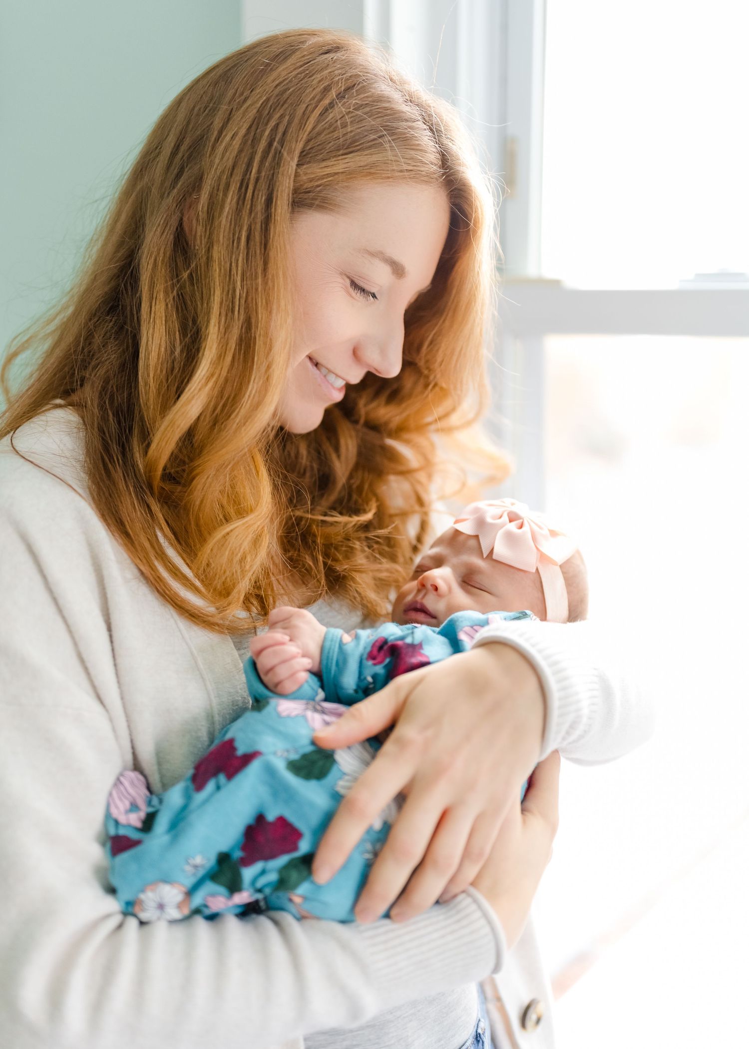 A tender moment between parent and newborn by a bright window.