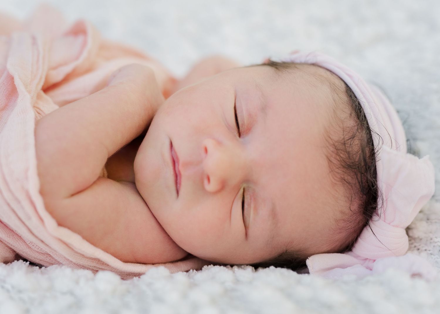 Sleeping newborn baby in pink swaddle resting on white textured blanket.