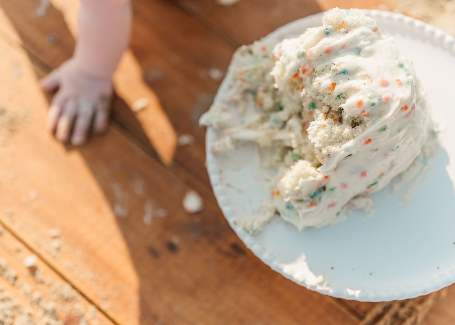 Hands mixing and kneading white dough on a wooden surface with scattered flour and plates nearby.