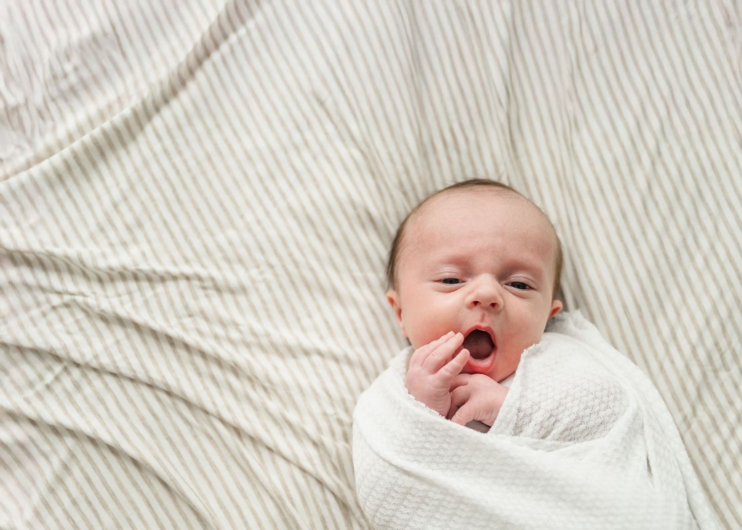 A sleeping newborn baby lies on white textured fabric with eyes closed and peaceful expression.