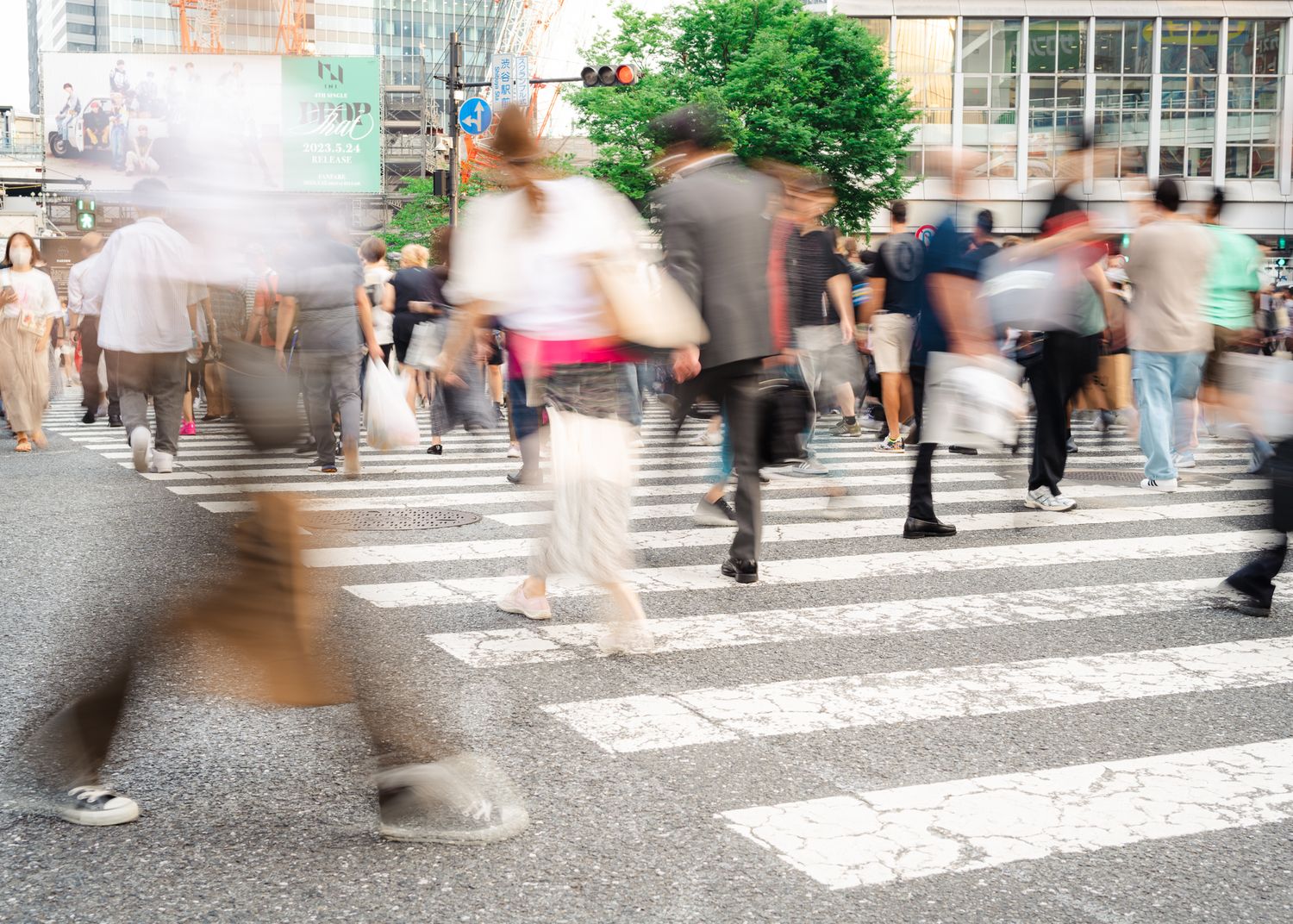 Motion-blurred crowd crossing a busy urban crosswalk in Japan.