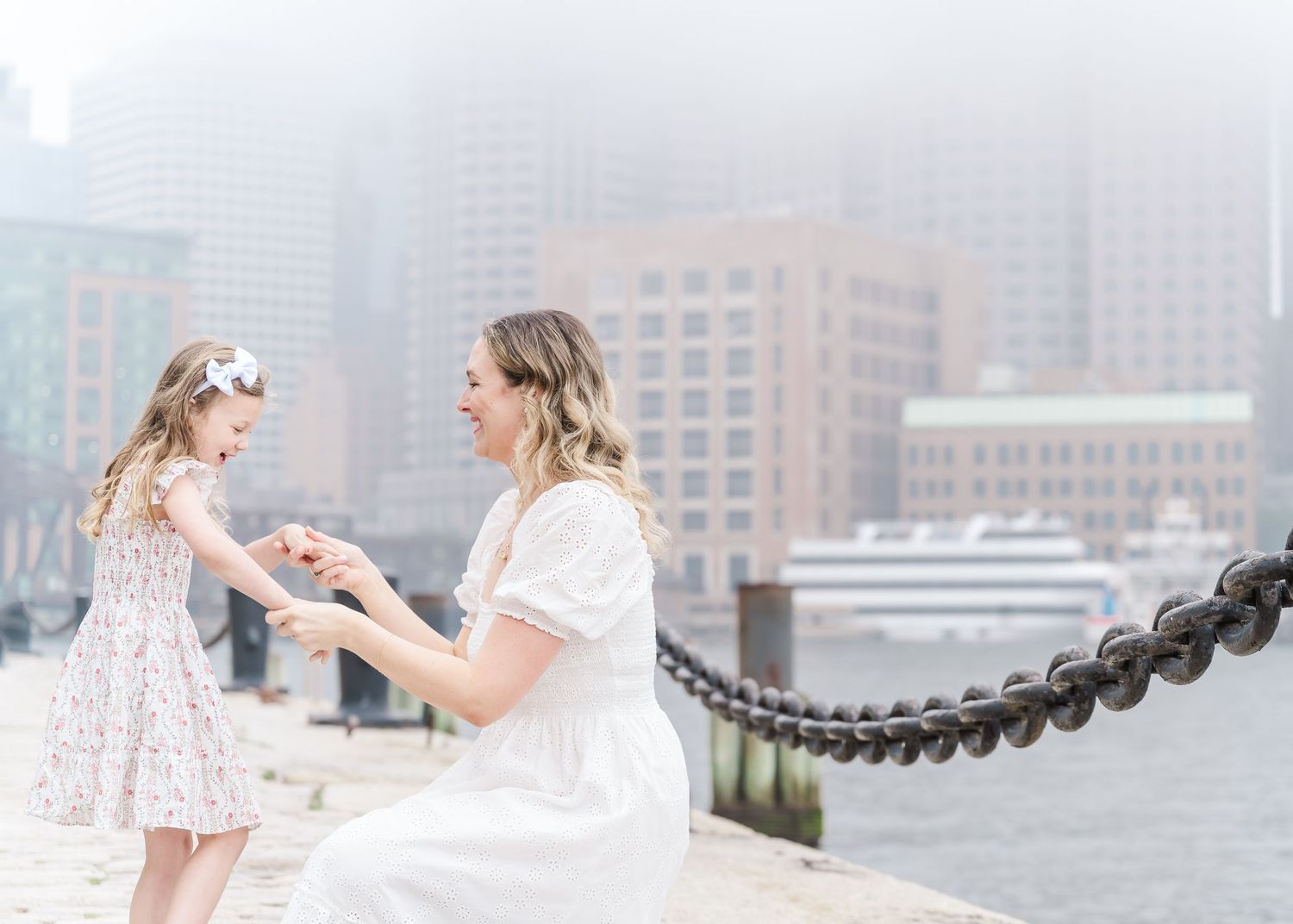 Two people interacting on misty waterfront with urban backdrop.