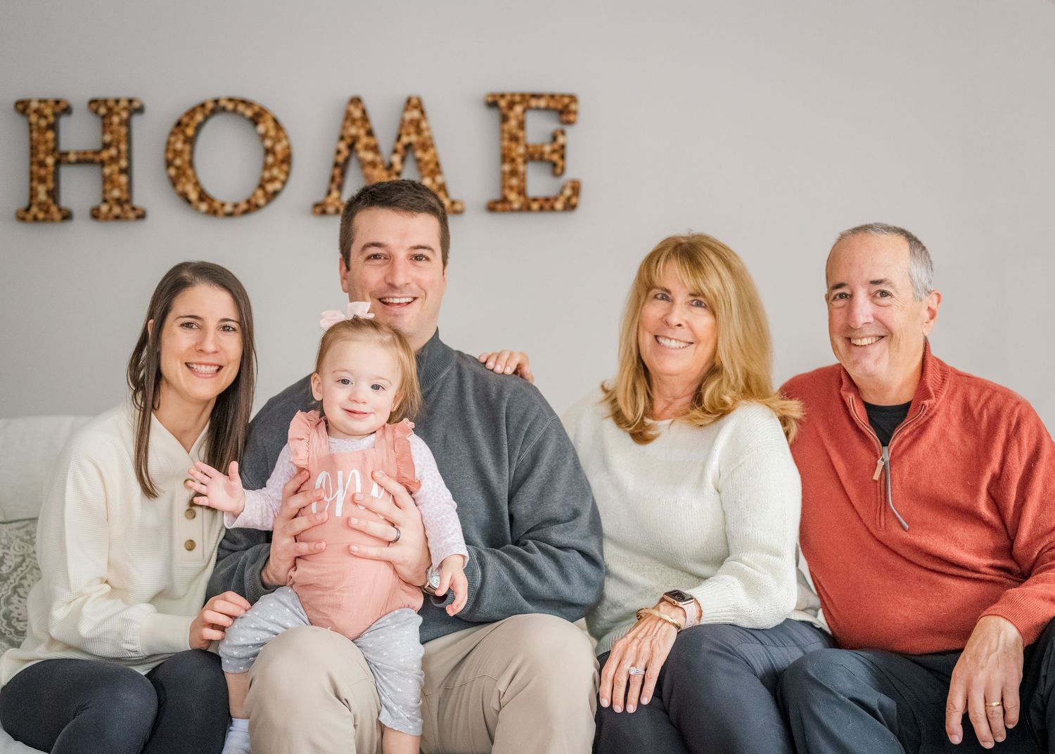Family photo with HOME marquee letters on wall in cozy indoor setting.