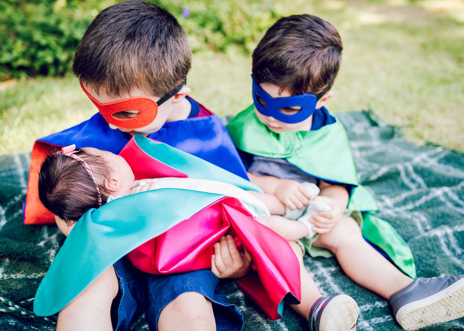 Children in colorful superhero costumes relaxing on a picnic blanket outdoors.