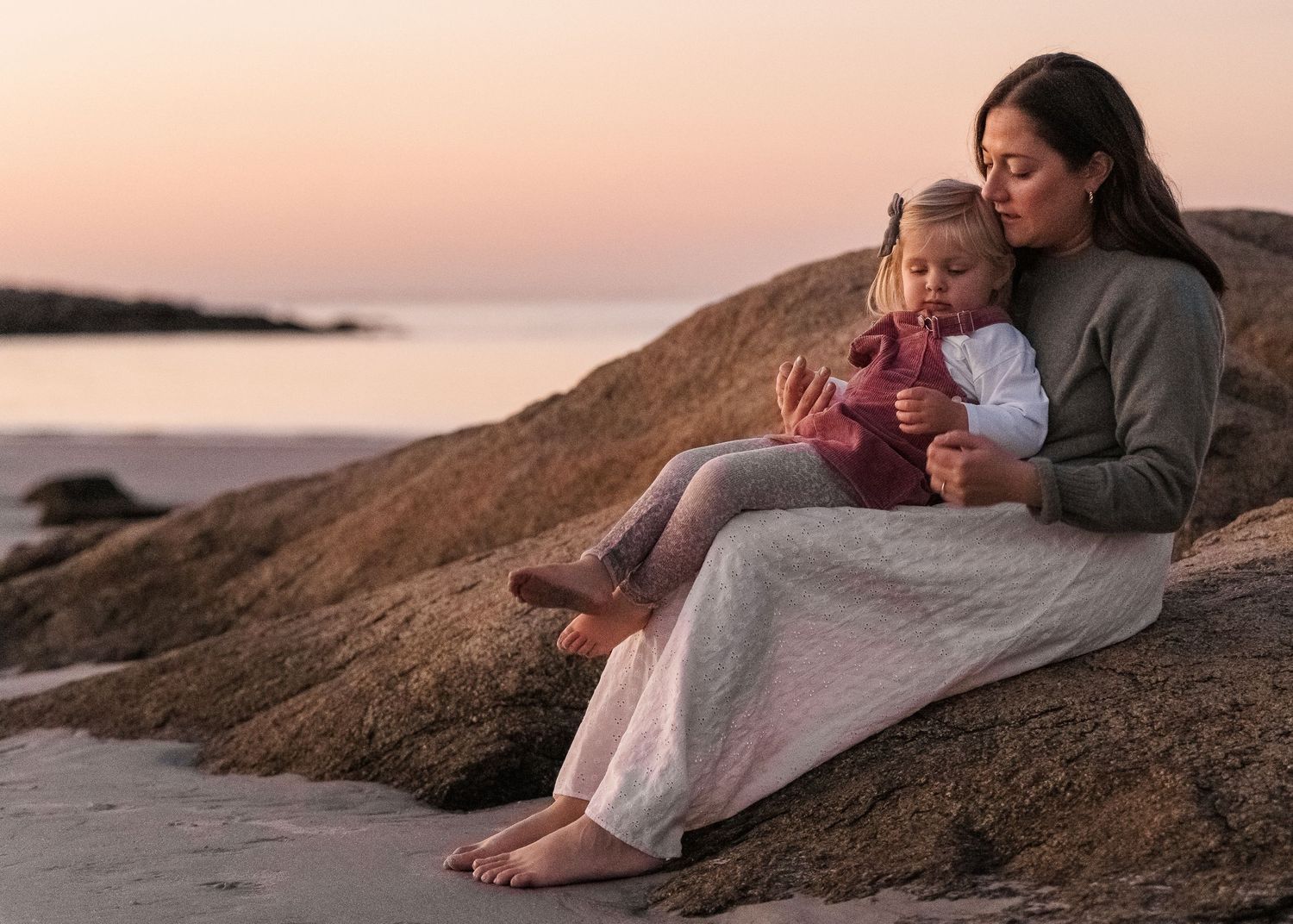 Couple enjoying a romantic sunset moment together on a sandy beach with coastal rocks in the background.