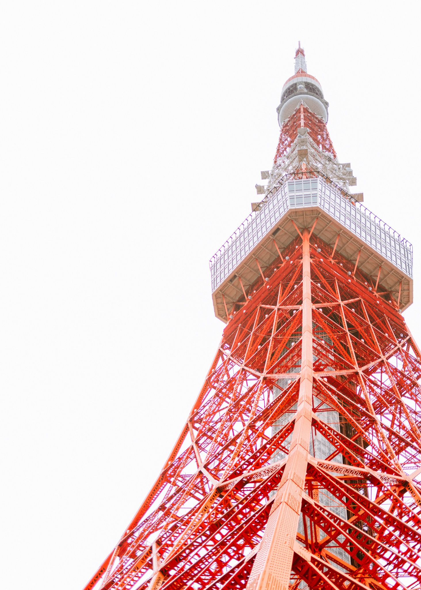 Low angle view of Tokyo Tower against white sky showcasing its iconic red and white structure.