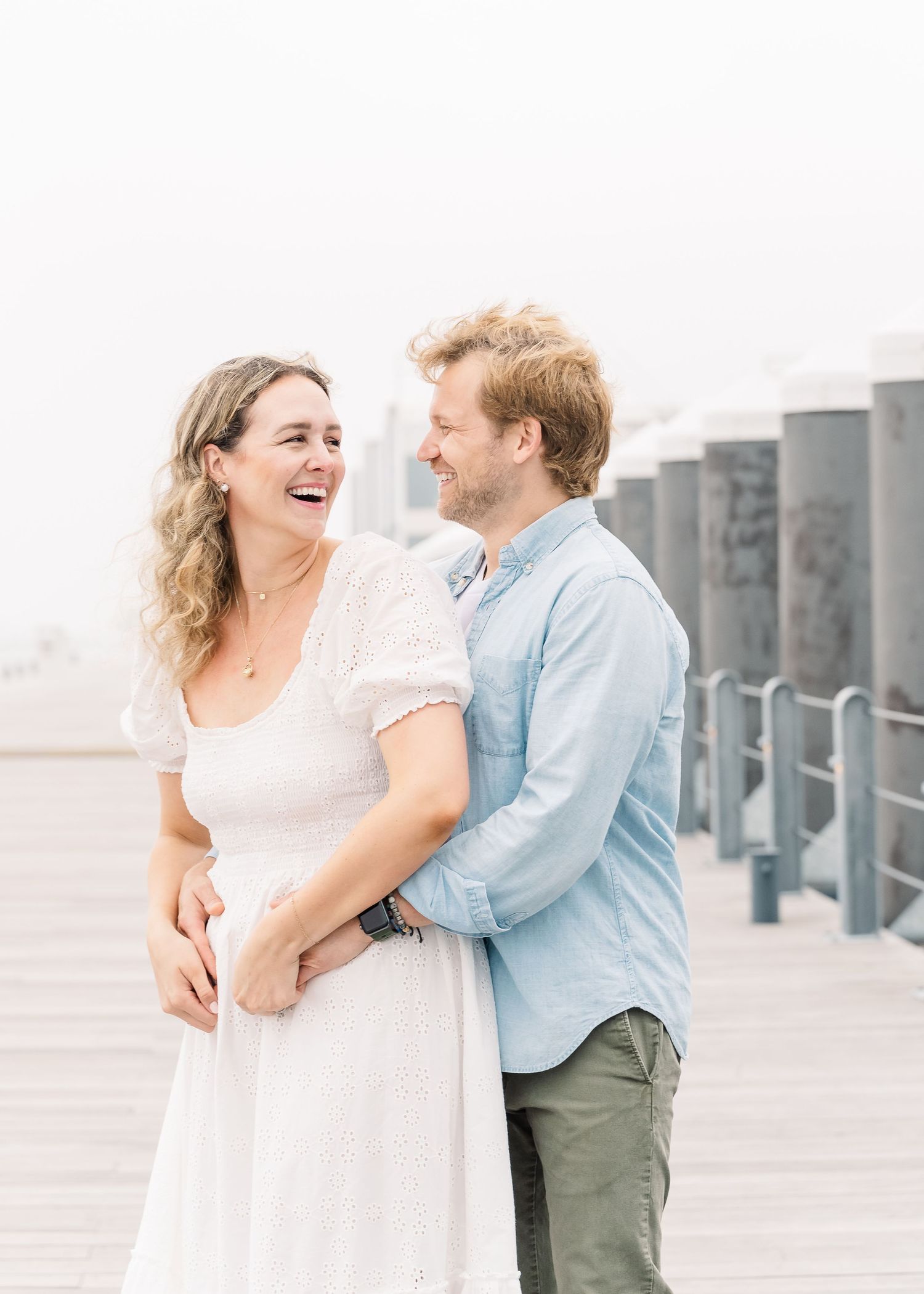Romantic moment captured on foggy waterfront with city buildings in background.