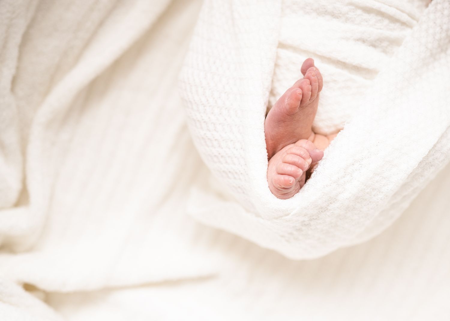 Tiny baby feet peeking out from soft white knit blanket.