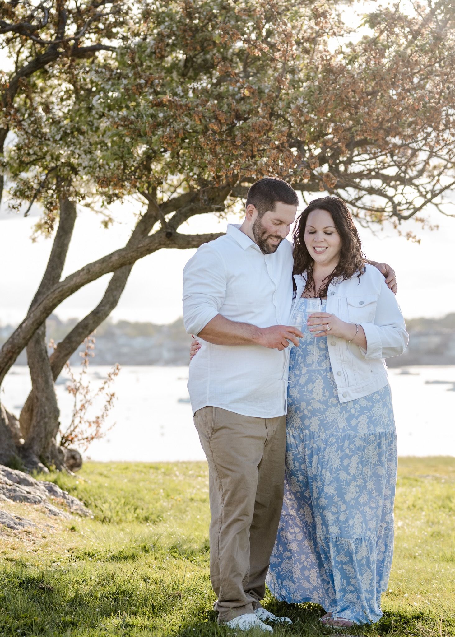 A couple shares an intimate moment under a flowering tree by the water.