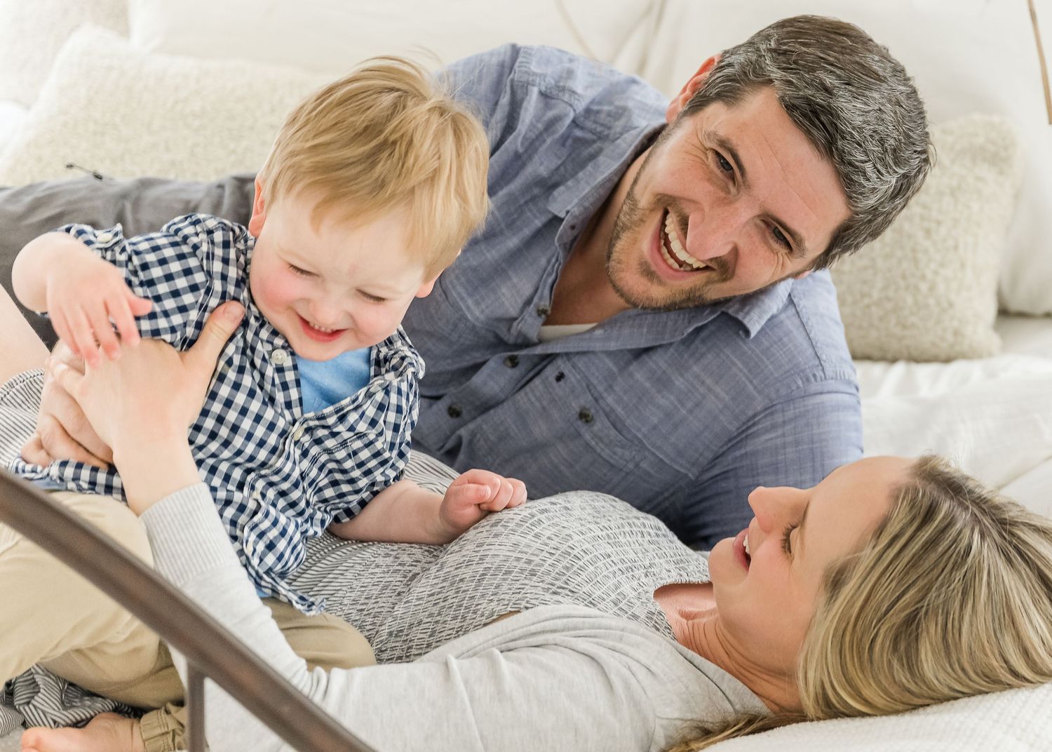 Happy family lying together on couch at home reading a book and sharing a joyful moment.