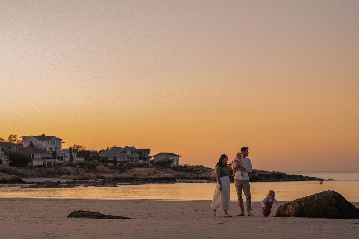 A panoramic view of beach houses along the coastline at sunset with silhouettes walking on the shore.