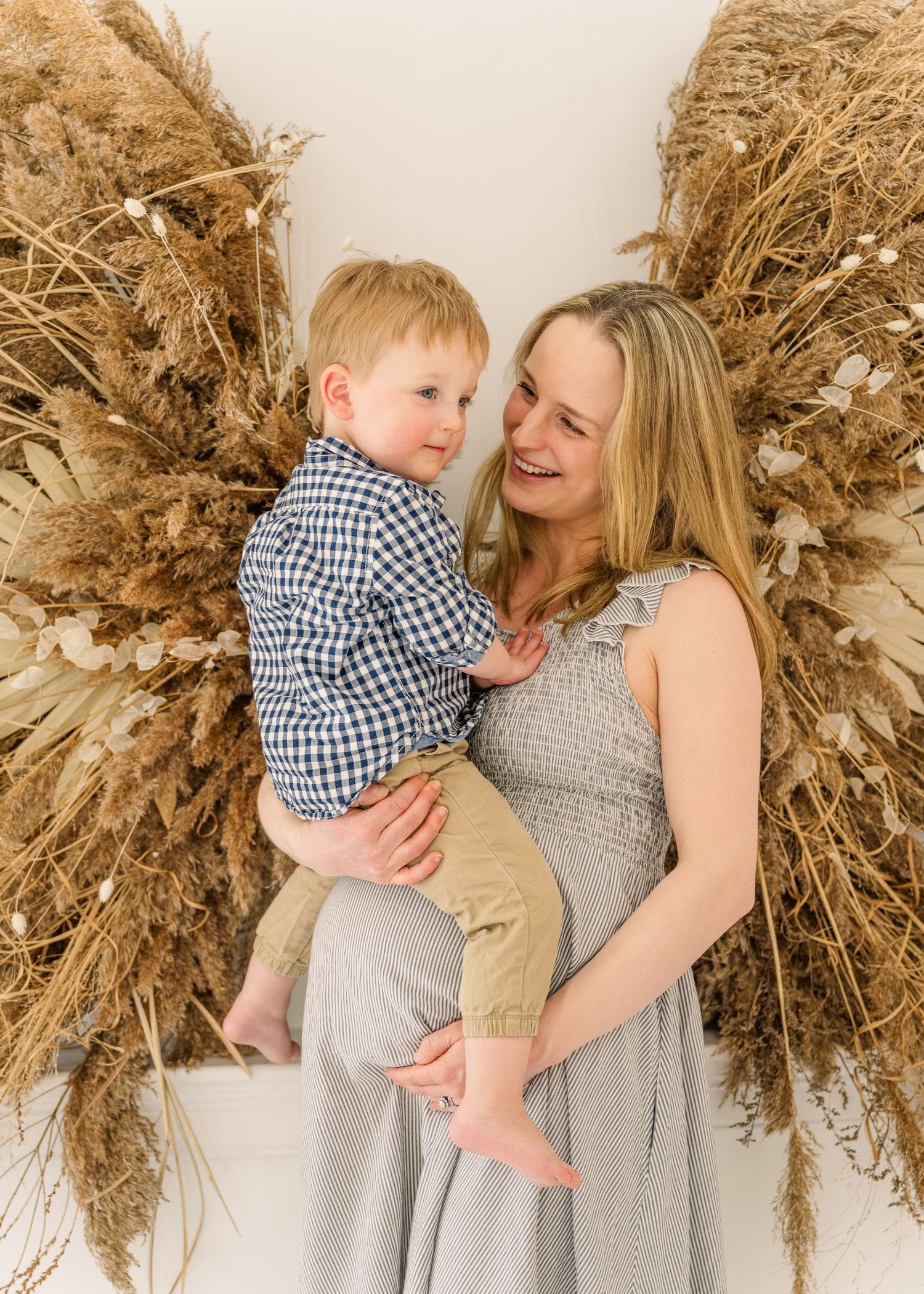 A child and adult share a sweet moment together in front of decorative pampas grass wall decor.