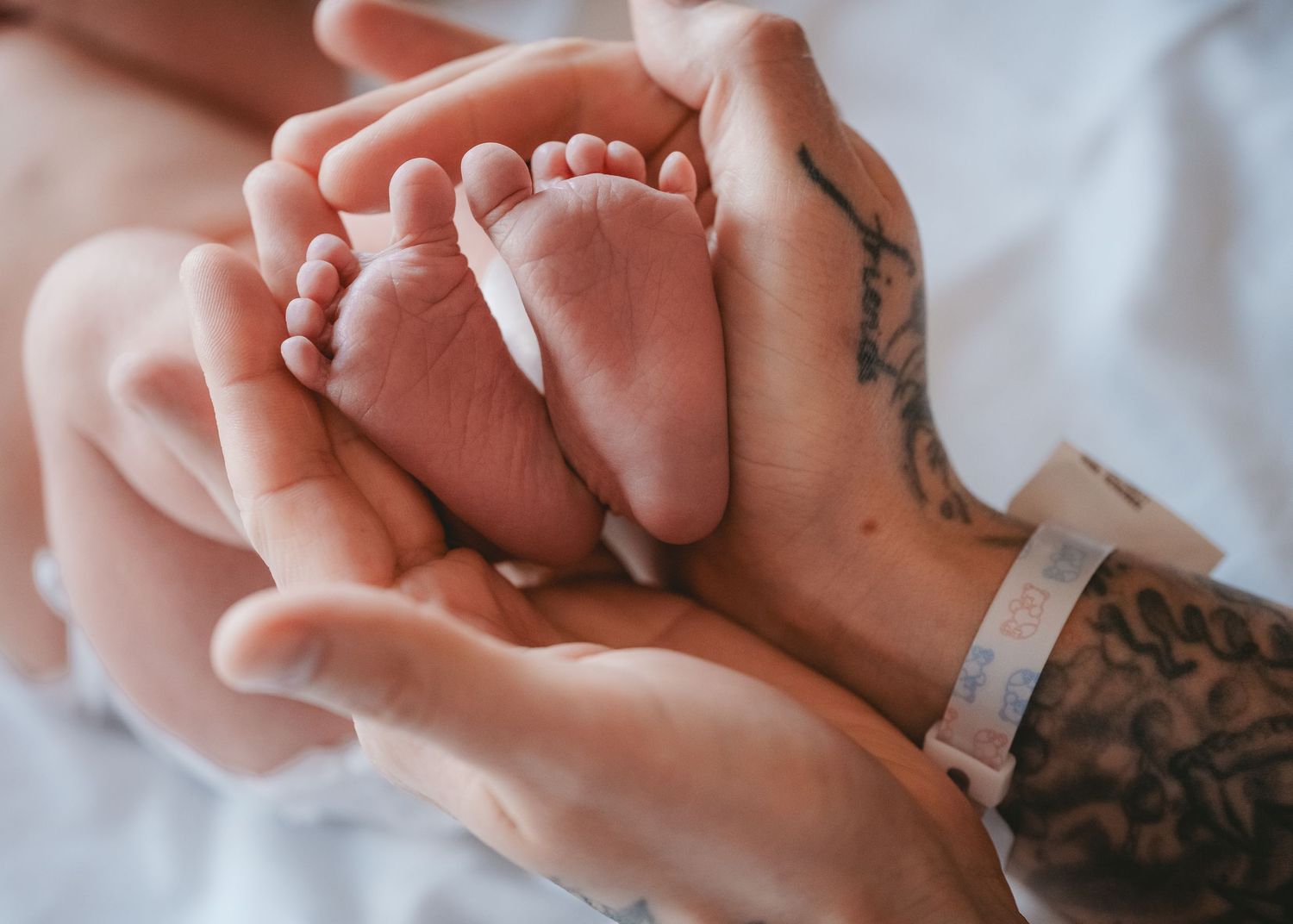 Close-up of tiny baby feet being gently held by tattooed hands.