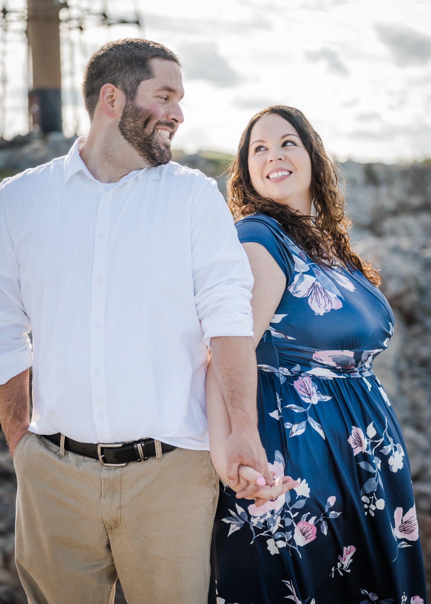A couple in coordinated outfits shares a loving glance while holding hands outdoors.