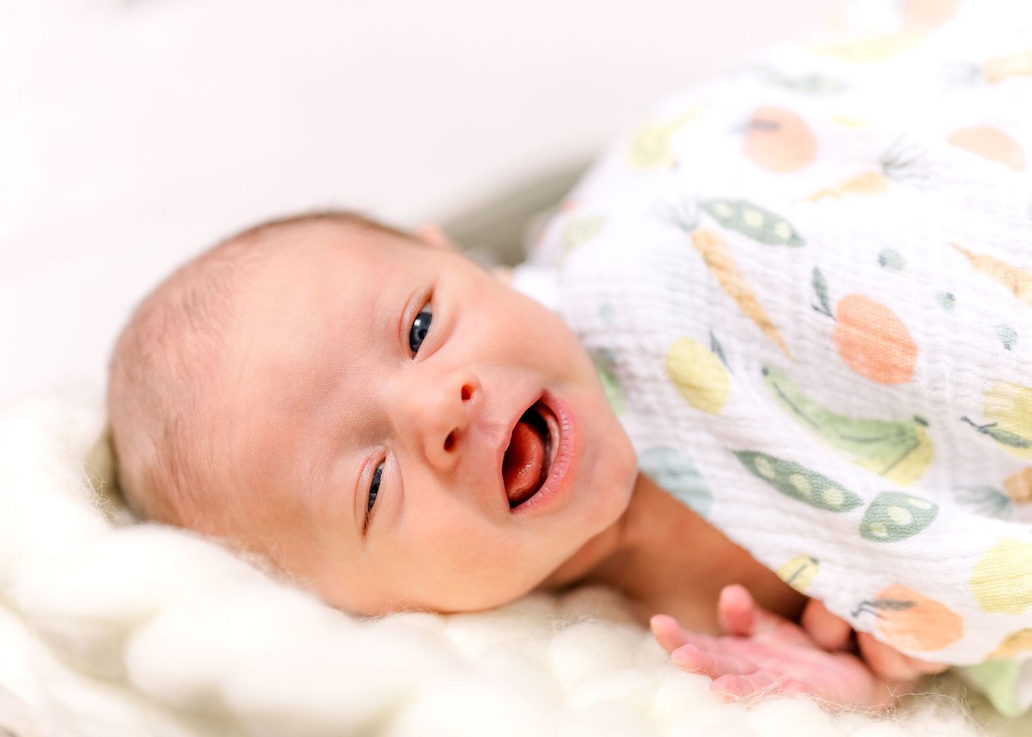 A laughing baby in floral print clothing lying on white bedding.