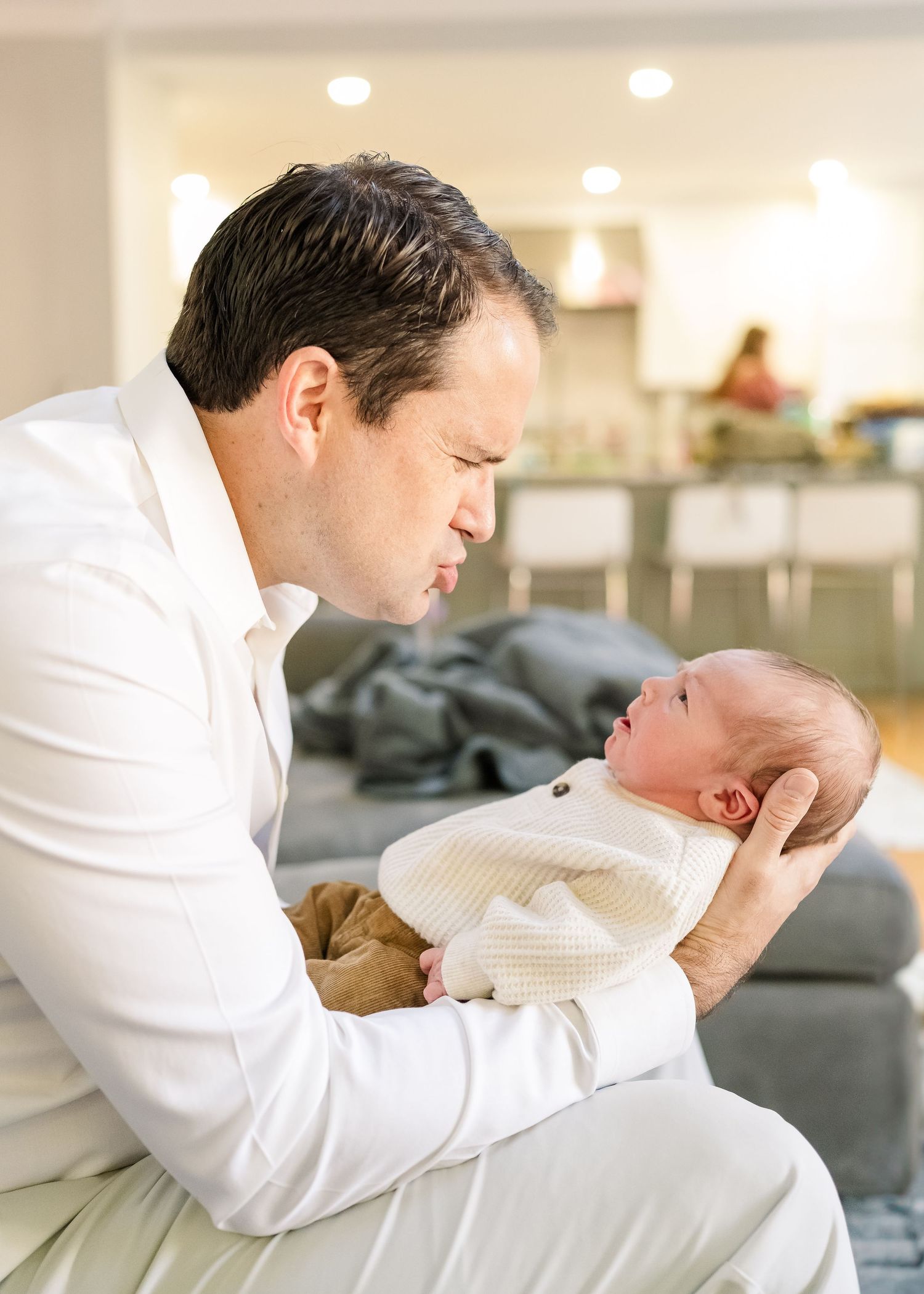 Tender moment between parent and newborn on grey couch in modern living room.