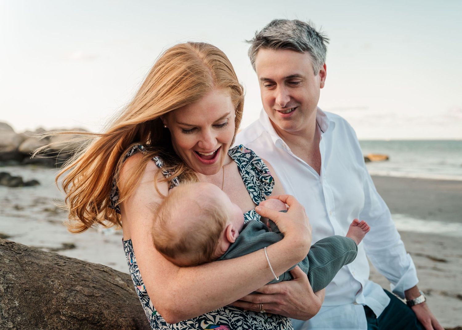 A joyful family shares a sweet moment together on a rocky beach at sunset, laughing and embracing.