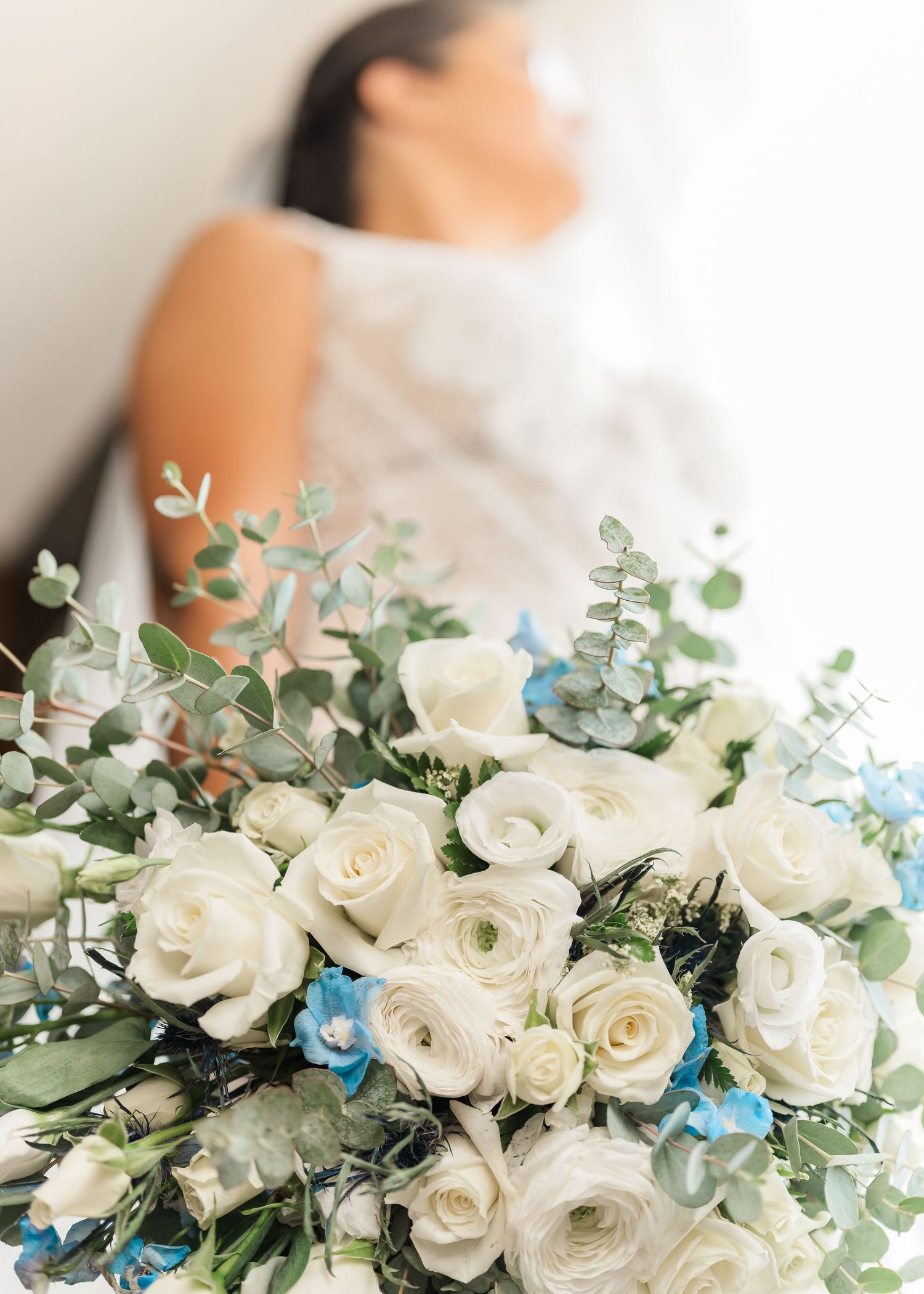 Elegant white rose bridal bouquet with eucalyptus greenery and delicate blue butterfly accents arranged for a wedding.