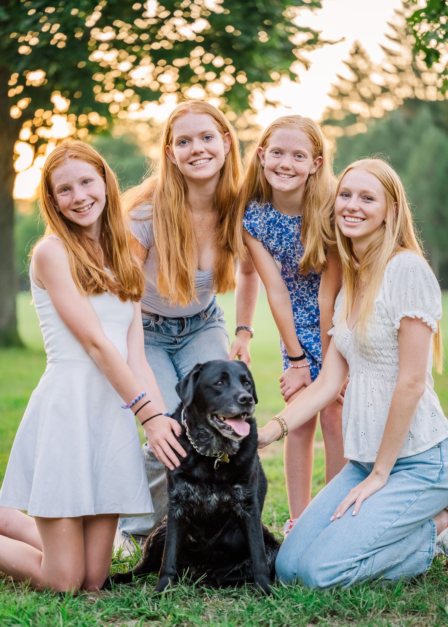 Four siblings pose with their black Labrador dog during a golden hour photo session.