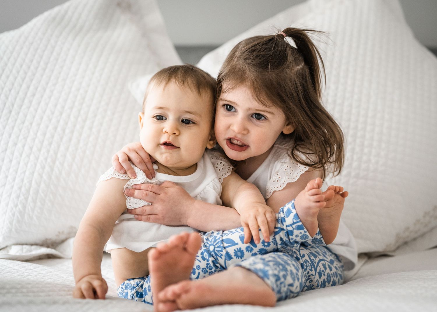 Two children sharing a tender moment while sitting on white bedding.