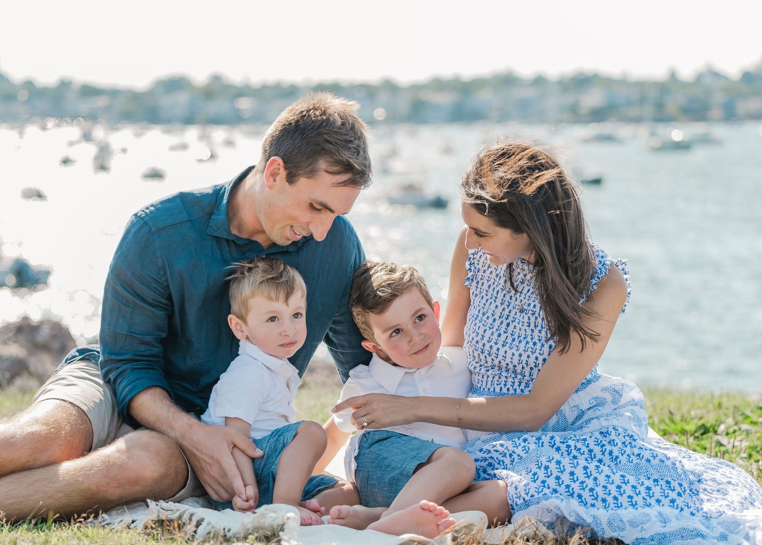 A family in blue and white outfits spends a sunny afternoon together by the waterfront with boats in the harbor.