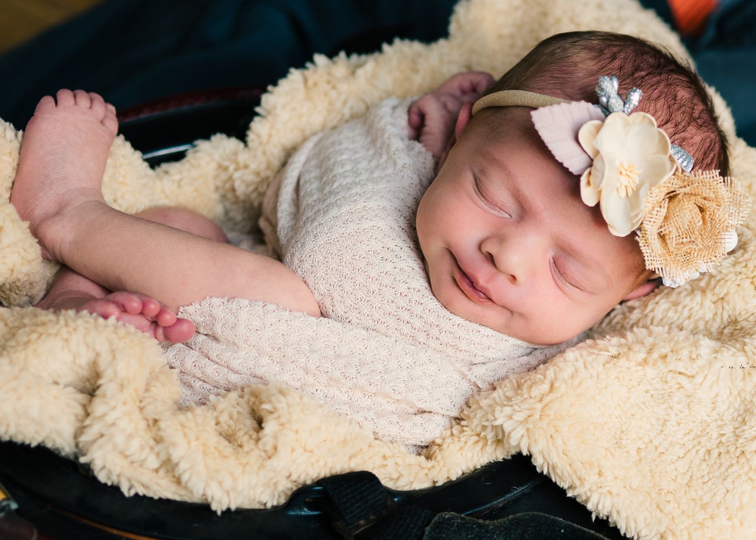 Peaceful sleeping newborn with floral headband lying on cream sherpa blanket.