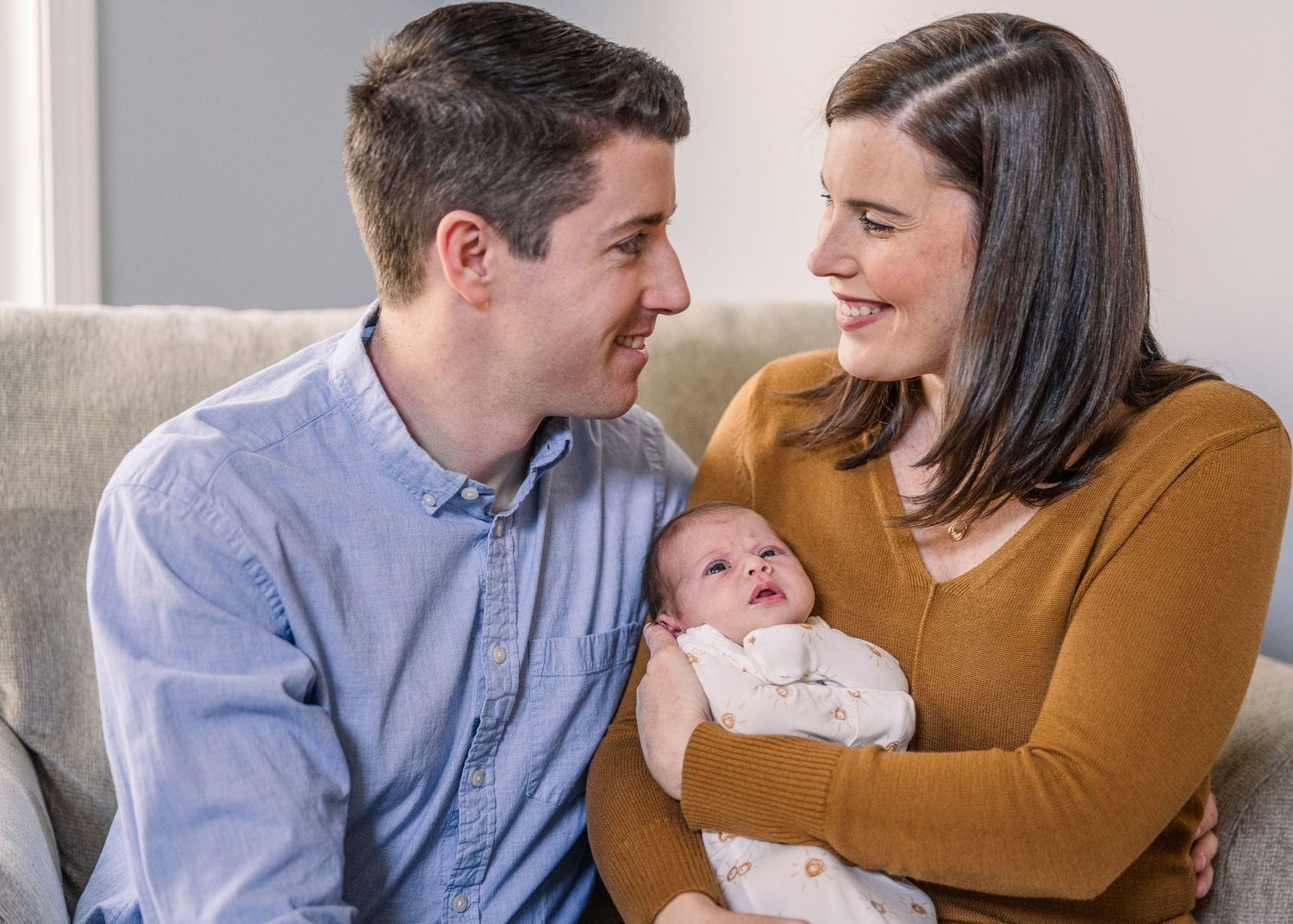 Happy family moment with parents cuddling their newborn baby on grey couch.