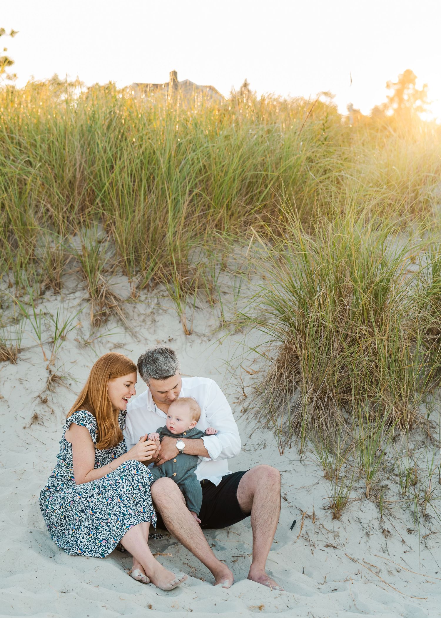 Family sits together on sandy beach dunes during golden sunset hour.