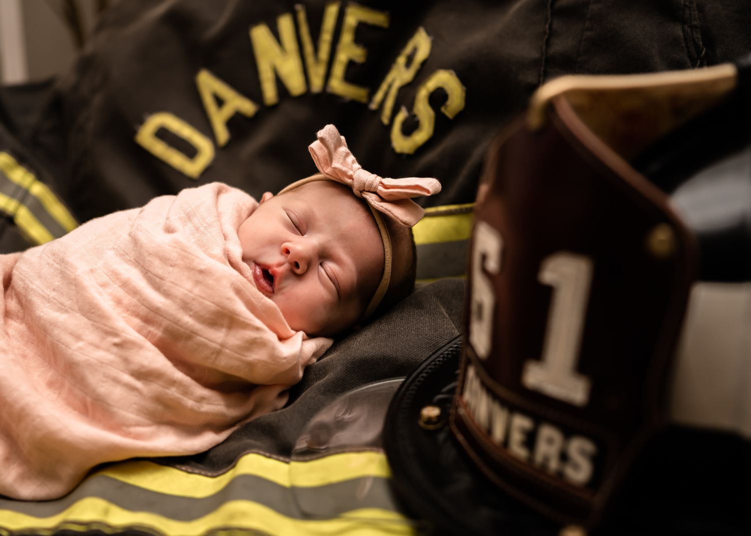 Sleeping baby in pink wrap on firefighter gear with Danvers text.