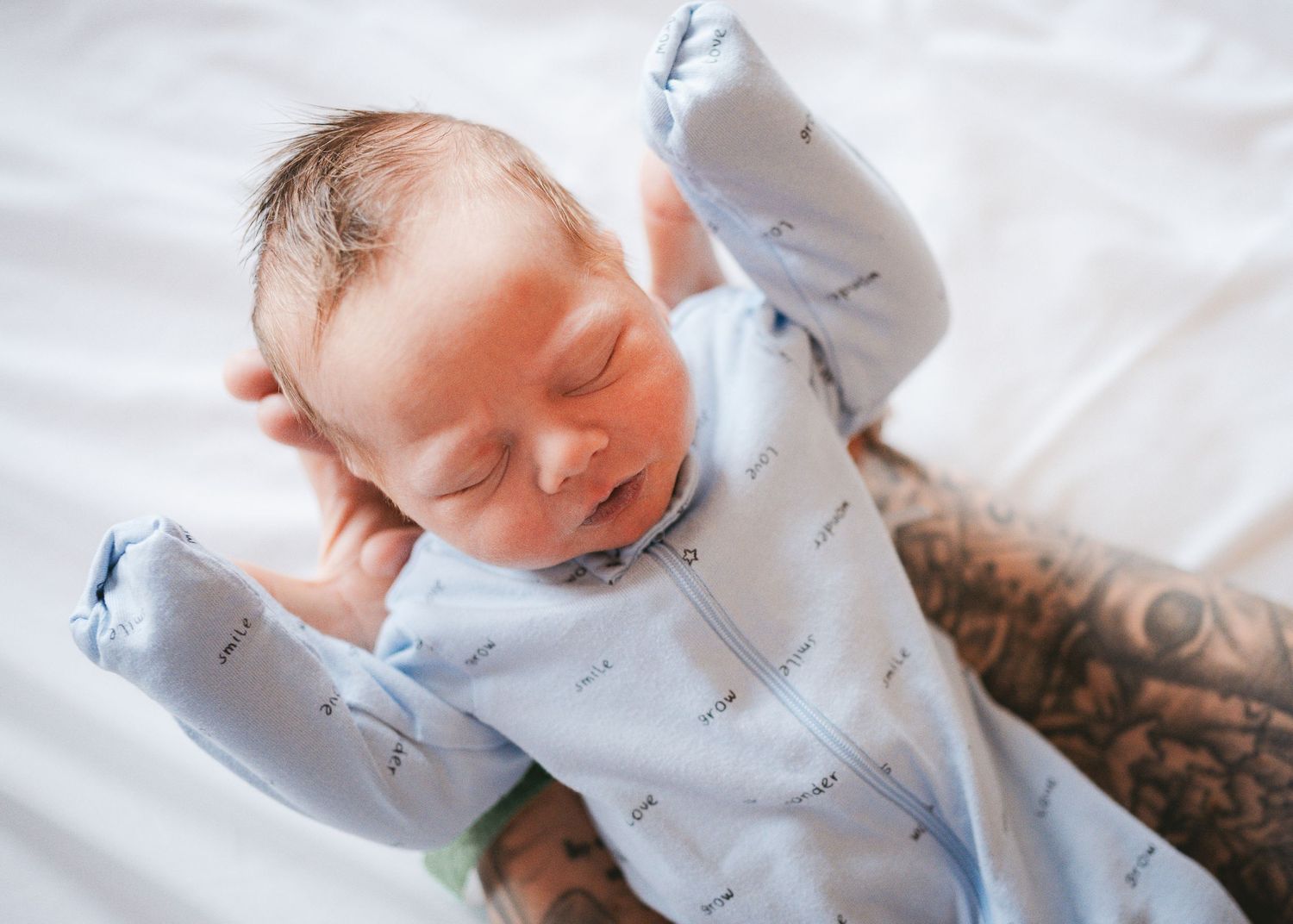 Peaceful sleeping newborn in blue patterned outfit on white bedding.