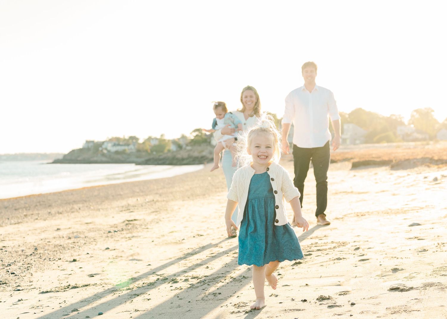Young family walking along a beach at sunset with long shadows.