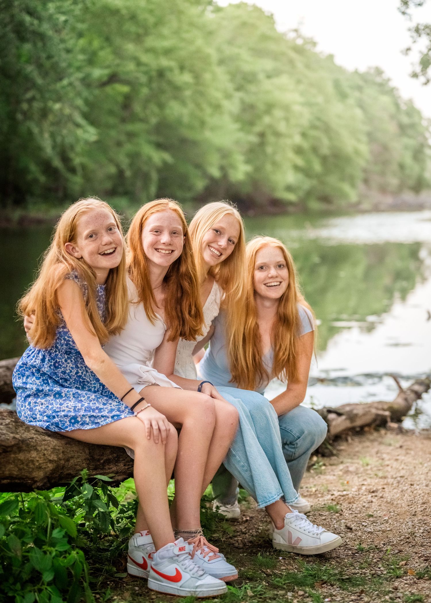 Four redheaded sisters sitting together by lake, wearing casual summer outfits.