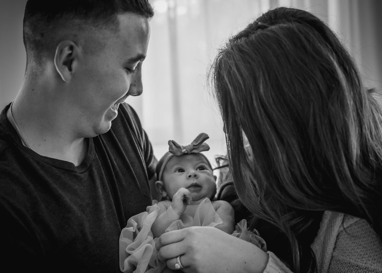 Black and white intimate family portrait with newborn wearing bow.