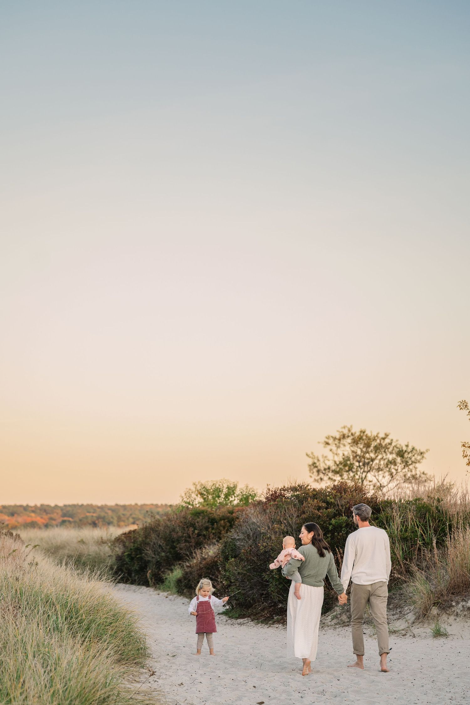 A family walking together along a winding sandy beach path during golden hour with coastal vegetation.