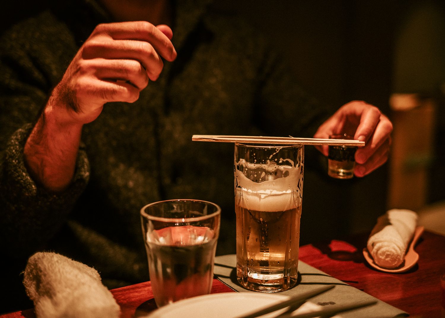 Two glasses of beer on a table with hands visible in warm lighting creating a cozy tavern atmosphere.