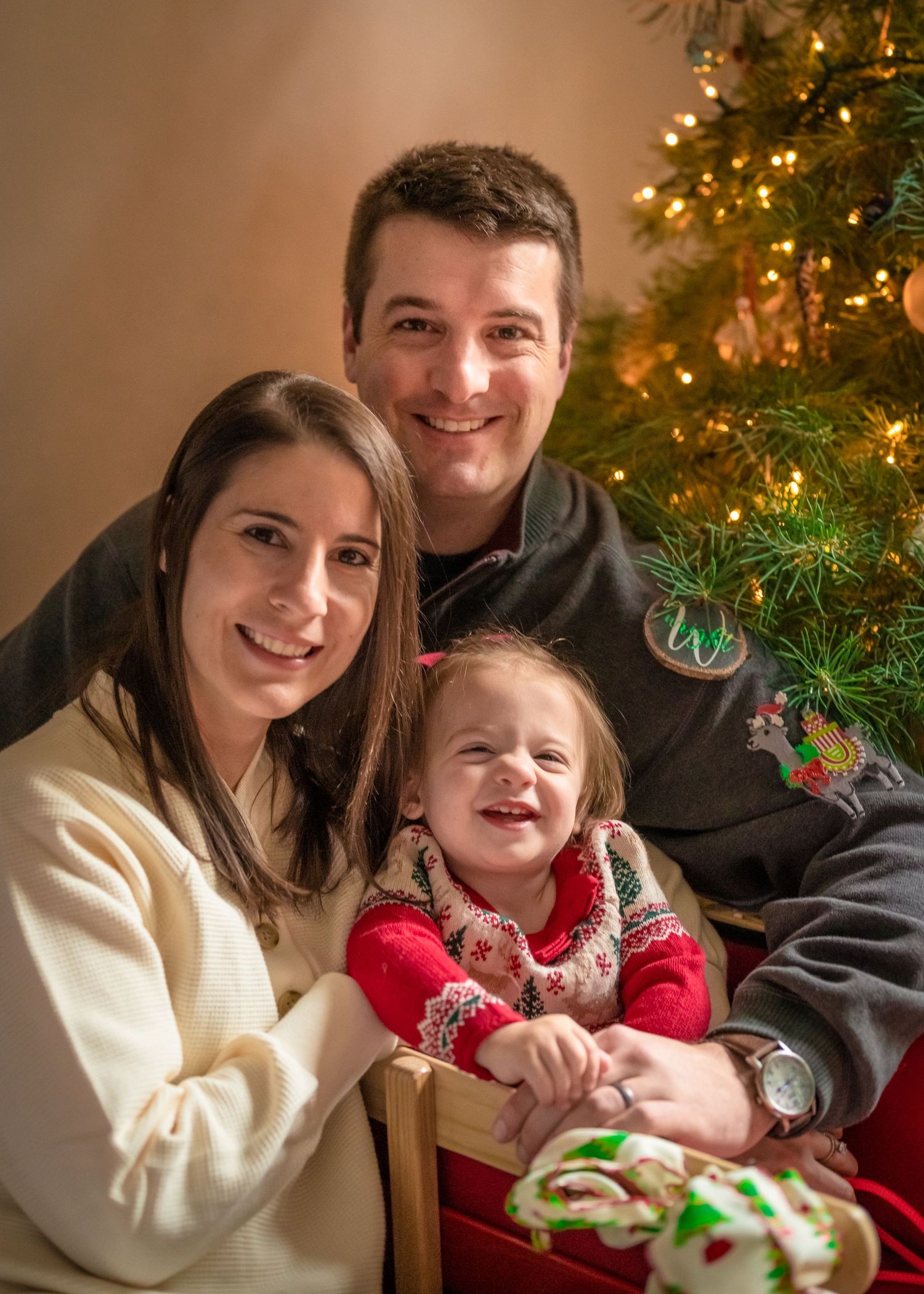 Family shares warm moment together by decorated Christmas tree during holiday photo session.