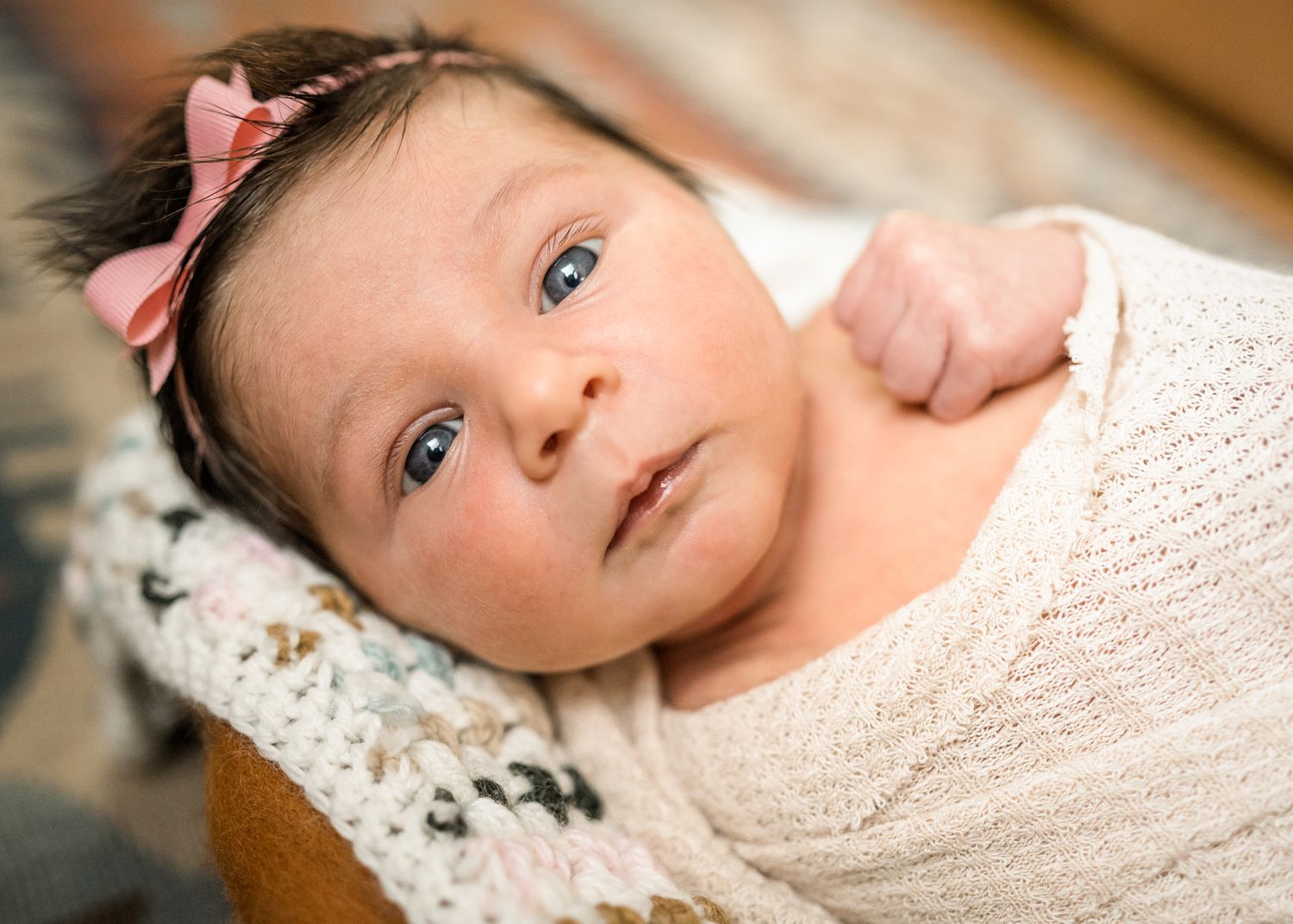 Baby wearing cream sweater and pink bow rests on lace blanket.