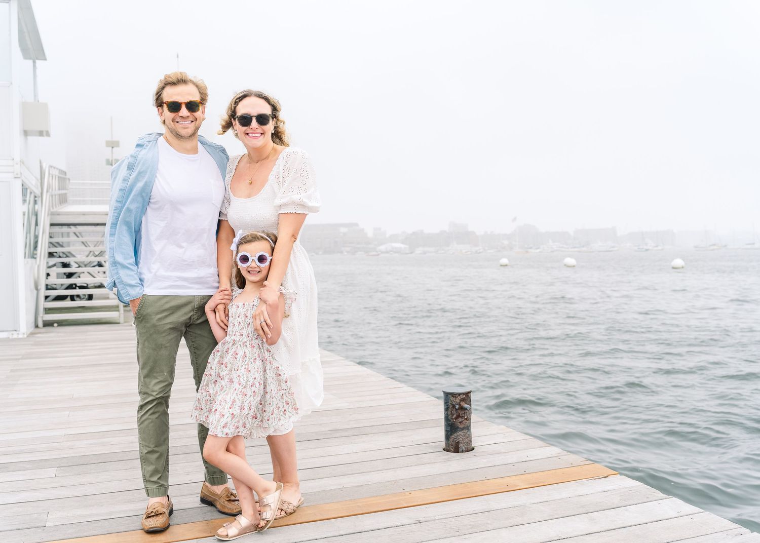 A family dressed in coastal style clothing poses together on a waterfront pier.