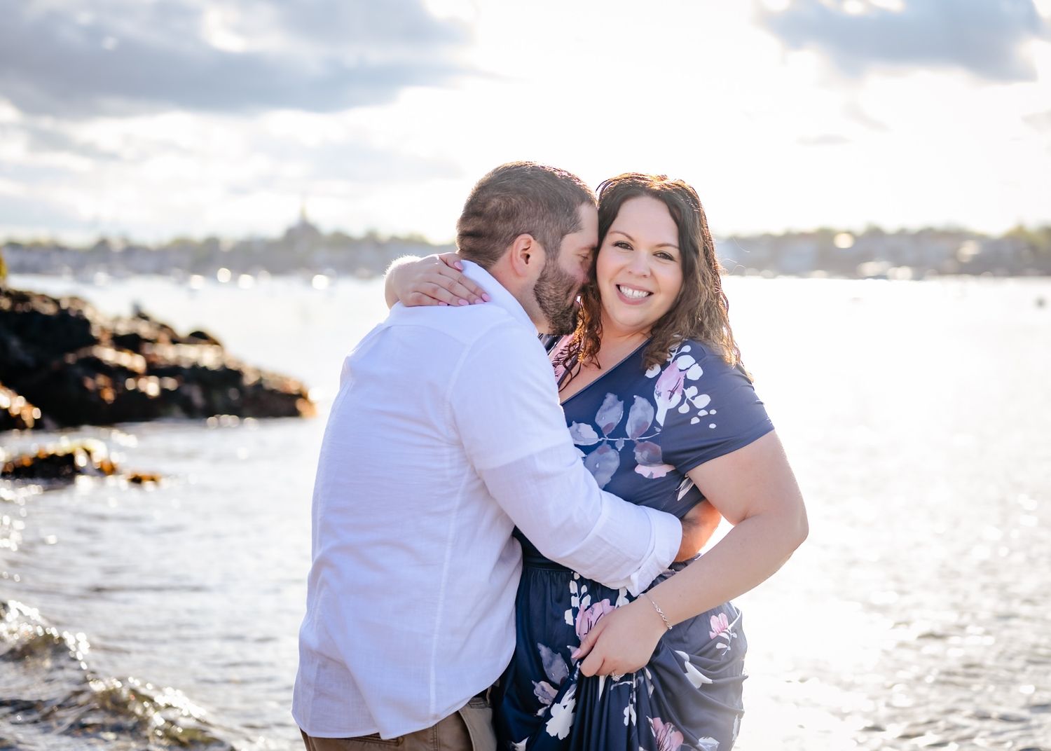 A couple shares an intimate moment along the rocky coastline during sunset.
