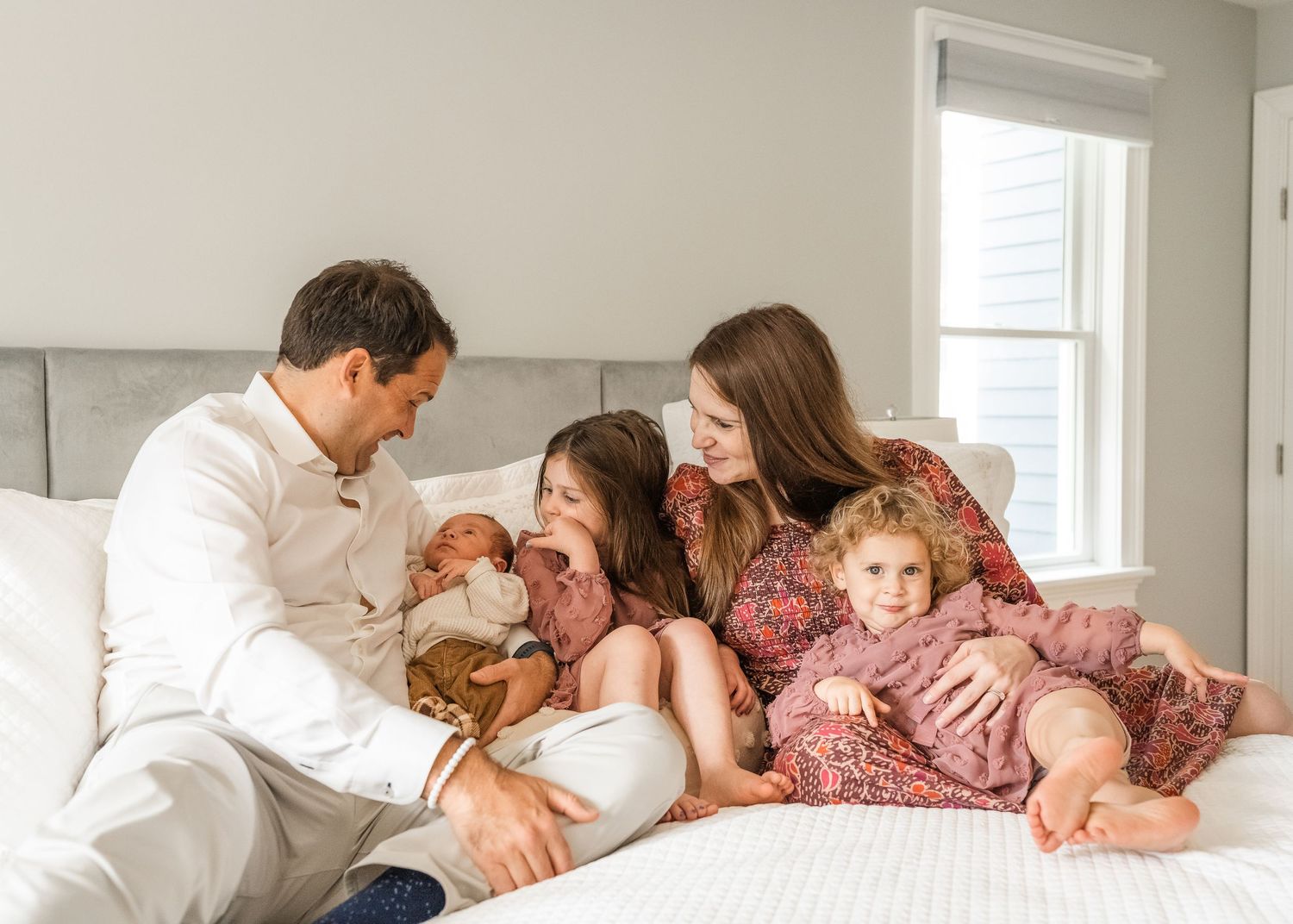Family lounging together on white bed in casual clothing sharing intimate moment at home.