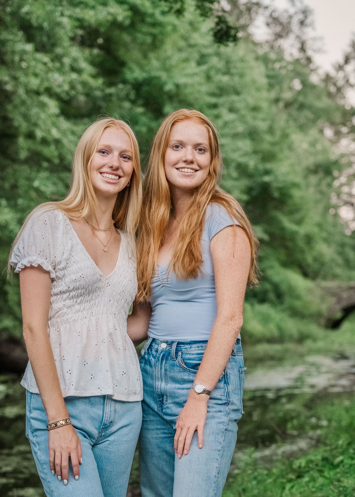 Two people with blonde hair pose together outdoors wearing jeans and casual tops.